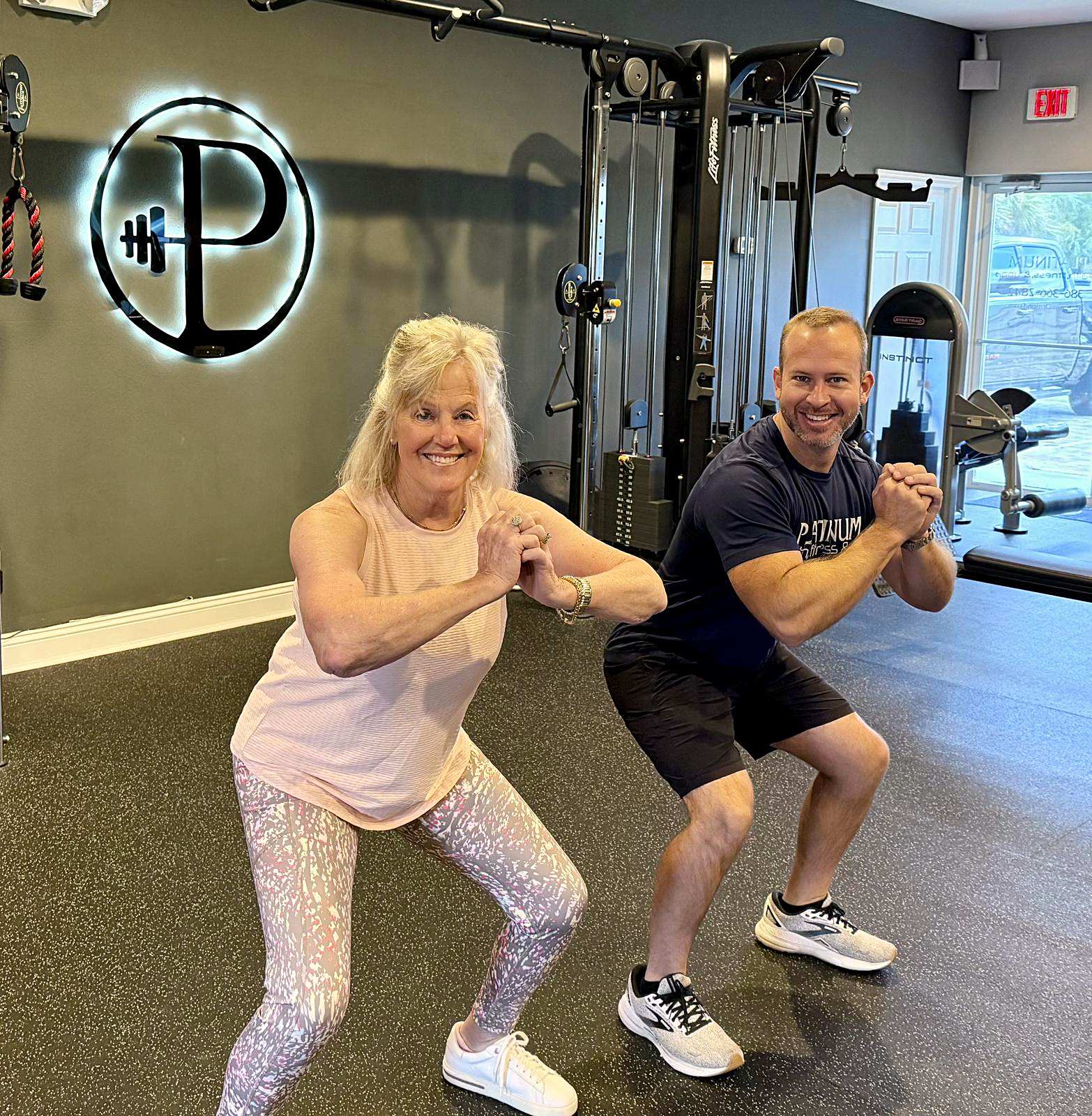 Travis Lightfoot coaching a client through a squat in front of the backlit P logo